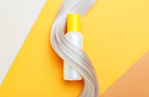 Shampoo bottle mockup strand in lock curl of blonde hair on orange color background. Yellow bottle shampoo. 