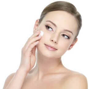 Portrait of young woman applying moisturizer cream on her pretty face