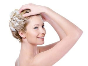 Beautiful smiling young woman washing her hair with shampoo