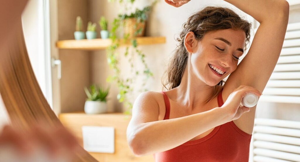 Beautiful young woman using deodorant under armpit in bathroom during morning time. Girl applying deodorant roll on after shower on underarms