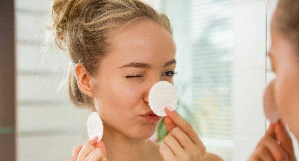 Young beautiful woman cleaning her face skin with cotton pad in bathroom.