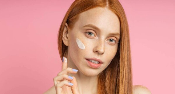 shot of young redhead woman applying foundation, face primer