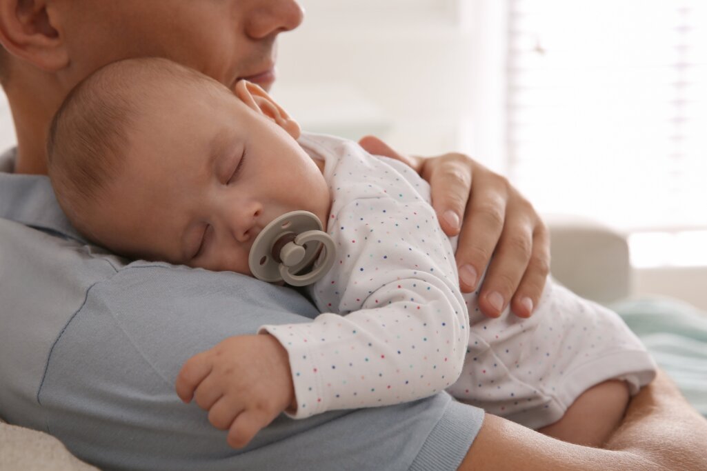 Father,Holding,His,Cute,Sleeping,Baby,With,Pacifier,At,Home,