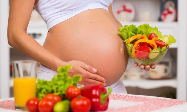 Close-up of a pregnant belly. Women's Health, fortified food. Fresh vegetables, diet and figure