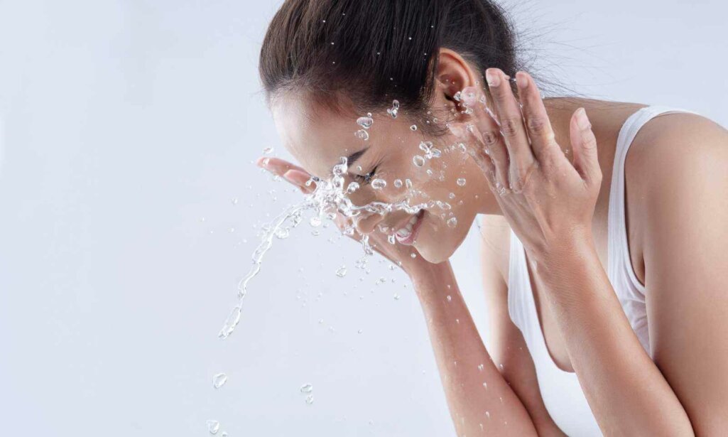 Beautiful woman washing her face in a white background studio