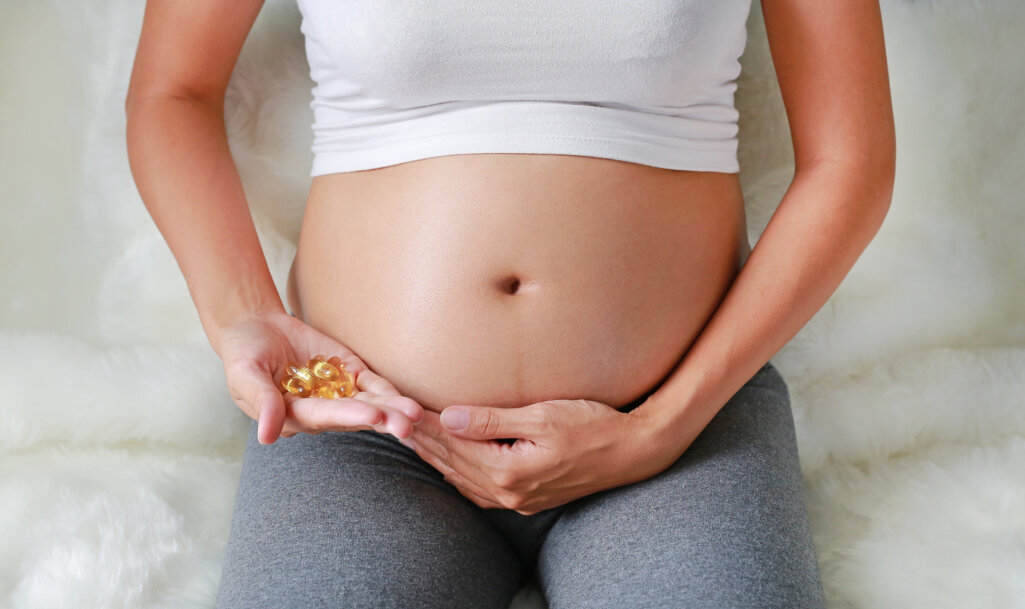 Pregnant woman holding fish oil tablets in a hand at her belly
