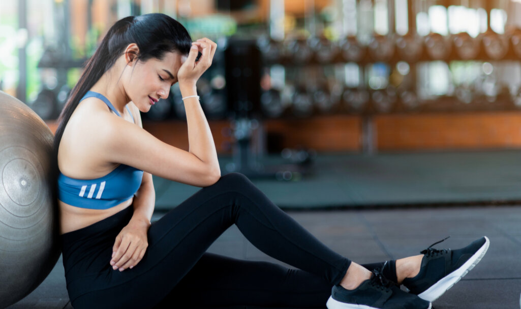 Tried asian woman is sitting on the floor after cardio workout.