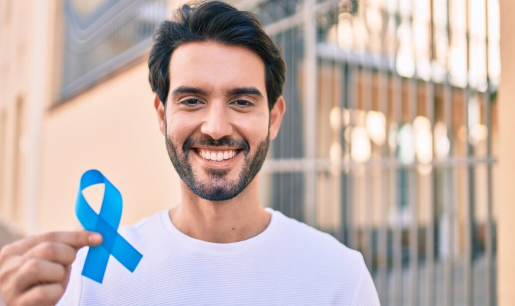 Young hispanic man smiling happy holding blue ribbon at the city.