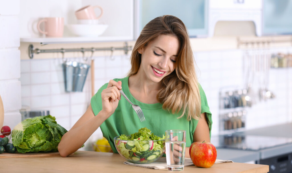 Woman eating vegetable salad at table in kitchen. Healthy diet