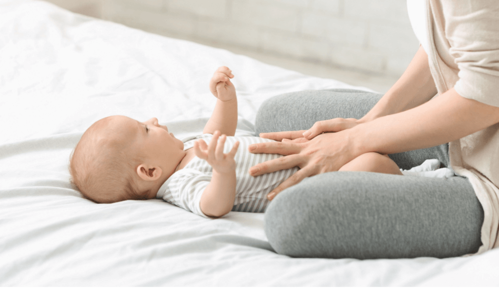 Baby healthcare. Woman massaging tummy of her son preventing colics, crop