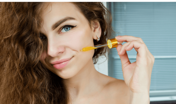 young beautiful curly woman uses yellow serum for face. The concept of facial skin care.