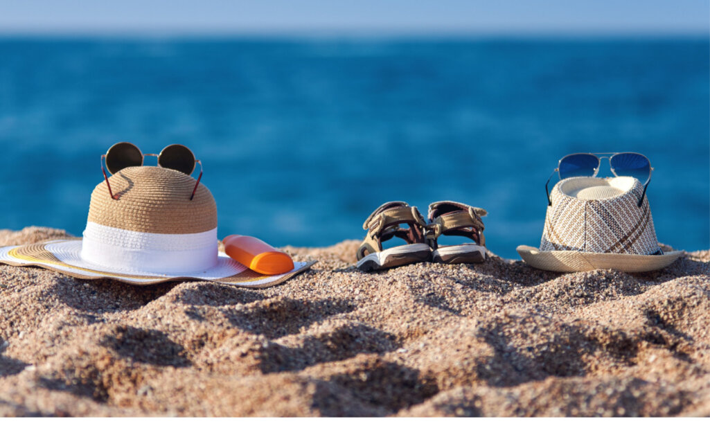 Family beach accessories. Fatherâs sunhat, motherâs bonnet hat, sandals of a child and bottle of sunscreen against the sea.