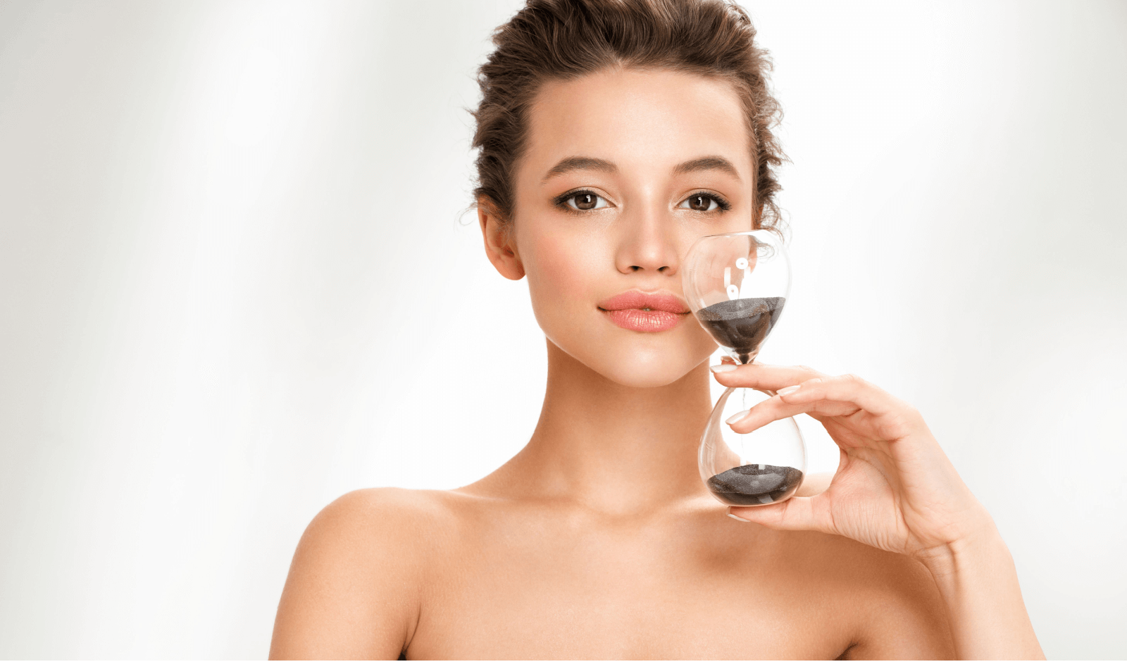 Woman holds hourglass. Photo of beautiful woman with perfect skin on white background. Beauty and skin care concept