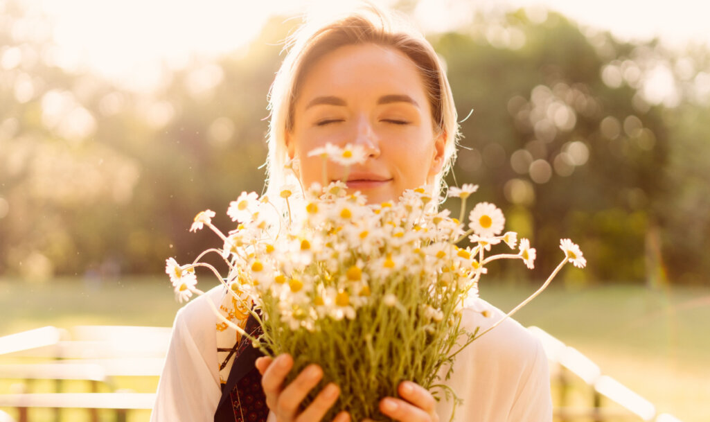 Γυναίκα μυρίζει ένα μπουκέτο με λουλούδια χαμομήλι. Κόνσεπτ της αξίας του χαμομηλιού στην υγεία του ανθρώπου.
