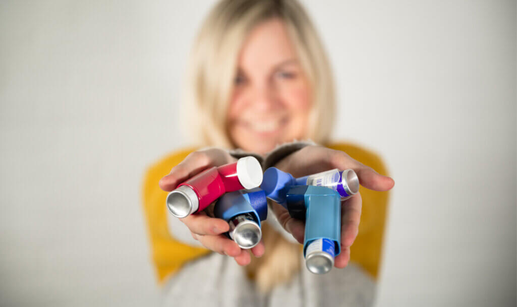 Young blonde woman holding various red and blue asthma spray inhalers in her hand
