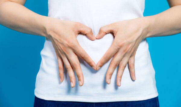 νεαρή γυναίκα που κάνει σχήμα καρδιάς με τα χέρια στο στομάχι της. Ενημέρωση για το μικροβίωμα εντέρου και πως συμβάλλει στην καλή λειτουργία του.