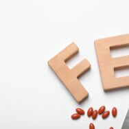 Wooden letters FE and pills on white background, top view. Anemia concept