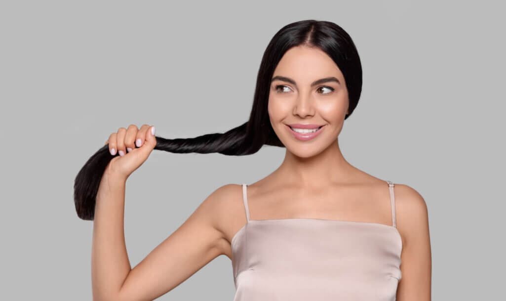 Portrait of beautiful young woman with healthy strong hair on light grey background