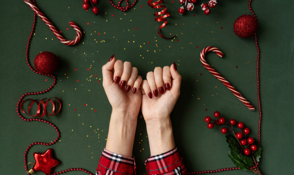 Christmas manicure. Red nails, hands in checkered shirt on green background with red christmas baubles as frame.